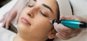Woman receiving basic microneedling treatment on her face, with a teal-handled device gently used